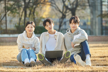 Three young college student male and female models sitting on the lawn at the university in autumn...