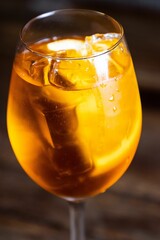 Clear glass tumbler filled with an orange liquid and ice cubes on a blurred background