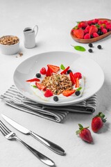 Vertical closeup of yogurt with granola and fruits on a white background