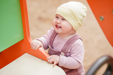 Cheerful baby toddler plays on the playground in the summer