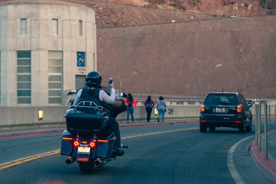 Hoover Dam, Nevada, USA - April 2017: A couple of bikers travel across America on a Harley Davidson motorcycle in Nevada near the Hoover Dam. Motorcycle passenger takes a photo on the phone.