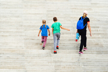 Mom, son and daughter are climbing a large, concrete staircase. The family walks along the city streets. Unrecognizable person. Back view