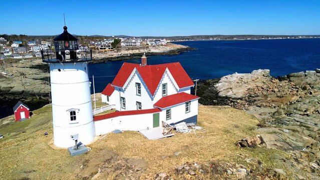 Rotating drone over Nubble Lighthouse over rocky cliff vy the sea in York, Maine