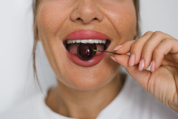 Woman with beautiful white teeth happily eats cherries