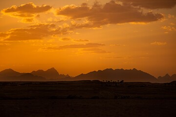 Orange sky with silhouetted mountains in the distance in a desert in Africa.