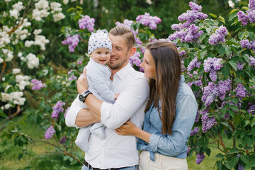 Naklejka premium Happy young family with a baby are relaxing in the spring blooming lilac park