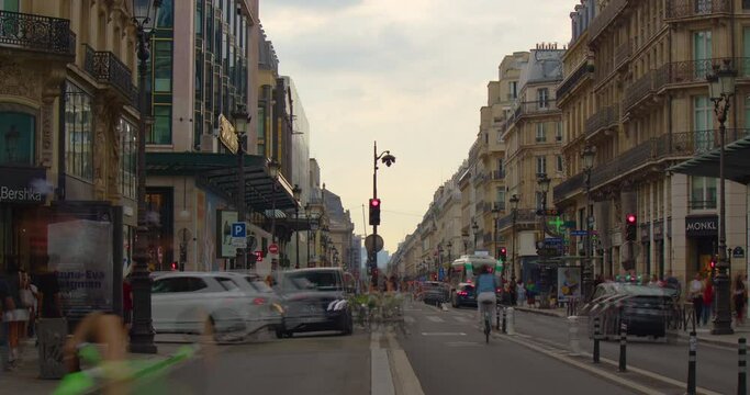 Many bicycles and pedestrians move along the main street of Paris. Main French street in Paris with cars and people. City traffic in the city, traffic lights and road signs. People rush to work