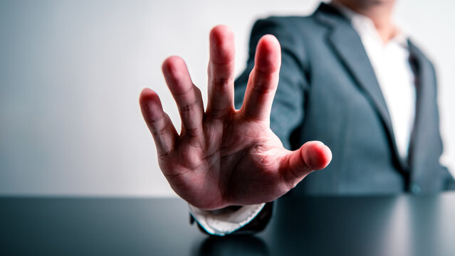 Businessman Raising Hand In Front Of Prohibiting Or Stopping Forbid And Invalid Gesture Sign On Black Table And White Background. Corruption Warning And Illegal Concept. Anti-corruption And Restrain.