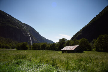 Mountain landscape with waterfall and wooden house in the middle of the valley