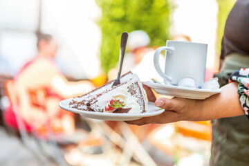 A waitress serving a piece of cake and coffee at an outdoor dining space in summer