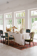 Table set for Thanksgiving with vintage chairs of different shapes and colors in a bright living room with French windows