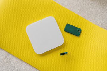 Scales, a smartphone and a fitness watch lie on a yellow yoga mat