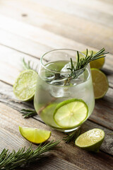 Gin tonic with ice, rosemary, and lime slices on an old wooden table.