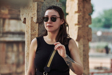 Attractive east asian woman in black sunglasses and black clothes stands among ancient pillars