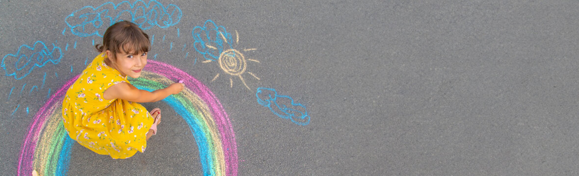 A child draws a rainbow on the asphalt. Selective focus.