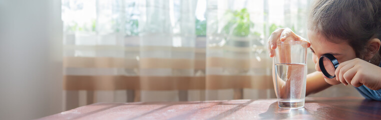The child examines the water with a magnifying glass in a glass. Selective focus.