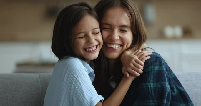 Close up portrait of happy family, young attractive mother cuddles daughter smile looking at camera, enjoy happy motherhood and priceless time together, spend time weekend at home, show love and care