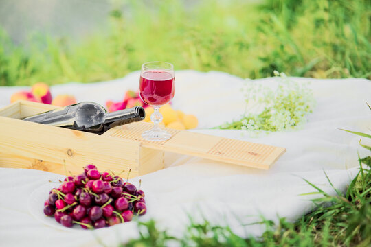 Still Life at a Picnic. Ripe cherry glass, wine, wooden box, bouquet of flowers layout on plaid