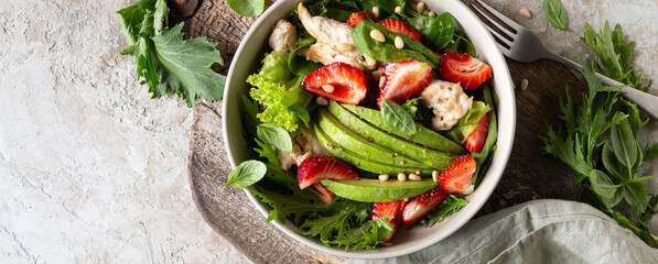 bowl with salad with chicken, avocado and strawberries on the table
