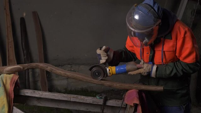 A worker in a protective mask cuts a half of a processed log with an electric tool to make a product. Handicraft work. Individual entrepreneurship. Startup. Small family business