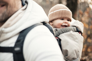 Sporty father carrying his infant son wearing winter jumpsuit and cap in backpack carrier hiking in...