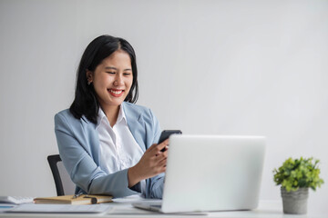 A smart and confident young Asian businesswoman or female banker in a formal business suit is on the phone with his client, dealing business over the phone while working in his office.