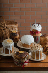 A lot of different Easter cakes with icing and decor on the table against the backdrop of a brick wall. Easter cakes and baskets