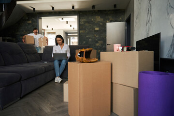 Girl is sitting on laptop while man is carrying boxes