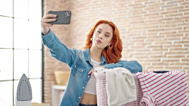 Young redhead woman making selfie by smartphone at laundry room