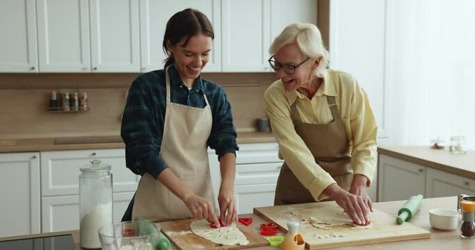 Pensioner 60s woman and young millennial daughter cooking together in domestic kitchen, enjoy conversation, using cutters to cutout cookies from homemade dough, prepare family recipe biscuits dessert