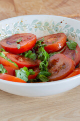Tomatoes and basil in a dish bowl with a balsamic vinegar and olive oil dressing. On a wooden worktop