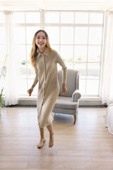 Happy teenager girl dancing at cozy home, enjoying activity, motion, childhood. Carefree beautiful dancer kid looking at camera, smiling, moving body to music. Vertical full length portrait