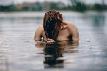 Portrait of naked woman swimming in a lake hiding behind hair