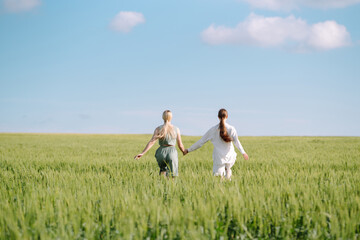 Two stylish women posing in a green field. Beautiful girlfriends in stylish clothes walk along the green field. Fashion, style concept. Summer landscape.