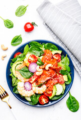 Fresh salad for keto diet with shrimp, salmon, avocado, spinach, cucumber, tomato, cashew nuts, sesame. Low-carbohydrate lunch rich in healthy fats. White table background, top view