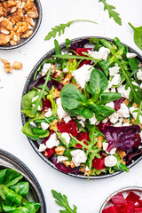 Beetroot and white cheese salad with arugula, lettuce, chard and walnuts, white table, copy space. Fresh useful vegetarian dish for healthy eating