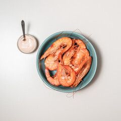 Shrimp in a blue bowl with sauce on the side on a white background