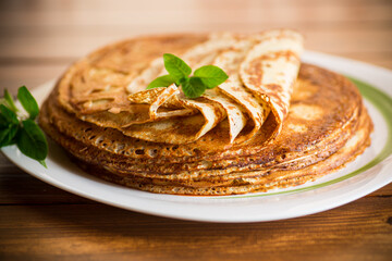 lot of thin pancakes in a plate, on wooden table.