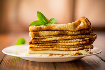 lot of thin pancakes in a plate, on wooden table.