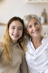 Happy beautiful grandmother and cute teen girl home vertical portrait. Cheerful granny and granddaughter posing for family picture with toothy smiles, looking at camera