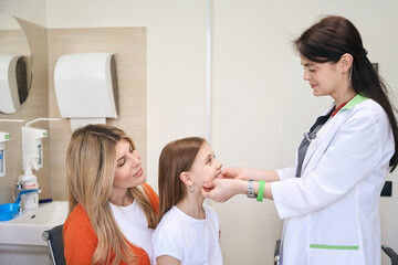 Little girl sitting on mother knees while pediatrician checking her lymph nodes