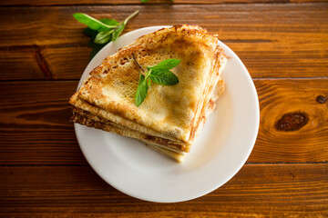 lot of thin pancakes in a plate, on wooden table.