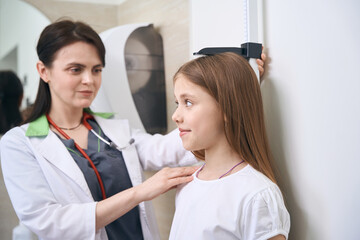Qualified woman osteopath checking girl height and posture
