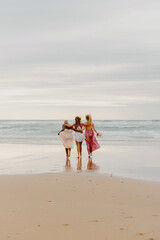 vertical photo on the beach of multiracial group of three young women walking towards the water....