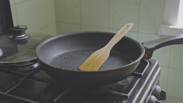 Dirty frying pan with wooden spatula stands on gas stove in kitchen room. Tools after cooking at home concept. Grease and oil stains