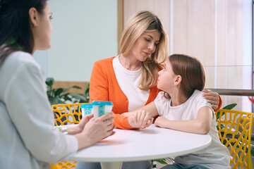 Obraz na płótnie Canvas Caring mother calming down little daughter talking to pediatrician