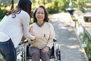 Obraz premium Asian senior woman in wheelchair with happy daughter. Family relationship retired woman sitting on wheelchair in the park age care at retirement home.