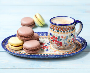 Obraz na płótnie Canvas Ceramic mug with coffee and macaron cakes on a blue background. Selective focus.