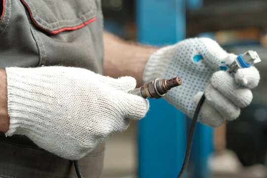 Car service. Maintenance and repair of a passenger car. A new oxygen sensor is in the hands of an auto mechanic. Control of the integrity and compliance of the spare part.