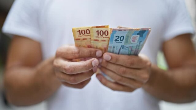 Young hispanic man counting mexican pesos at street